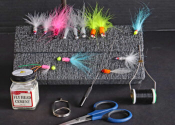 A small sampling of hand-tied crappie jigs, plus the necessary tools for tying. Left to right, the tools are head cement, hackle pliers, bobbin threader, bobbin and scissors.