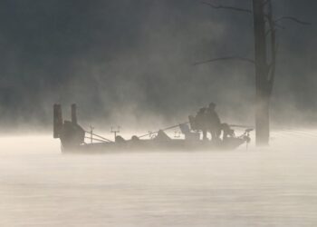 Silhouette of crappie fishermen spider rigging during an early morning fog